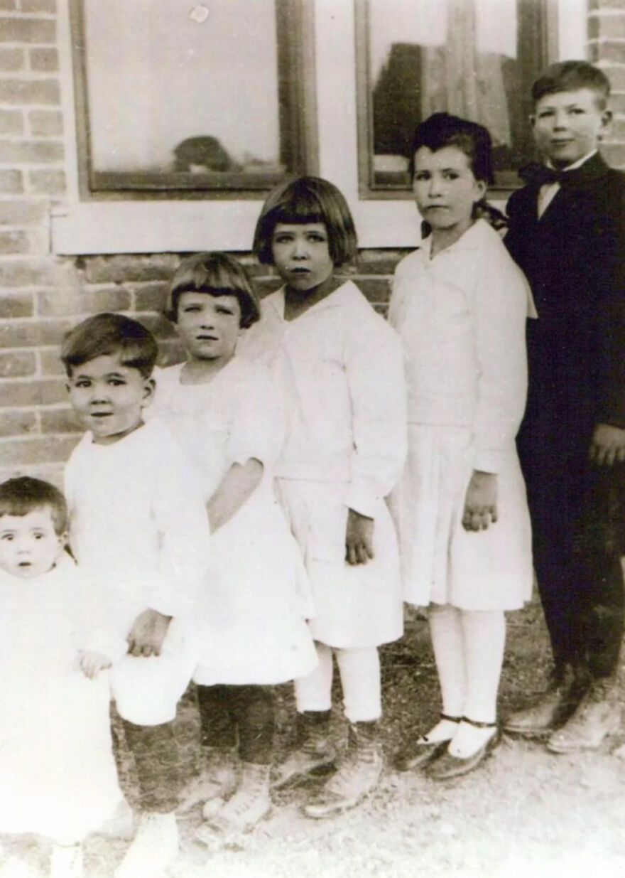 Vintage black and white photo of children standing in a row outside a brick building