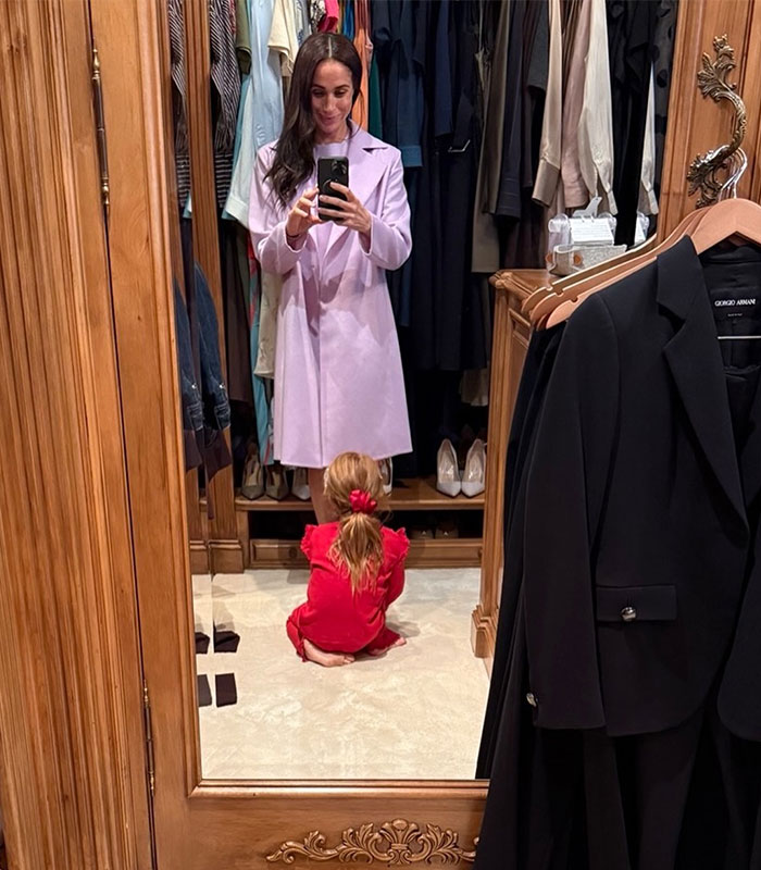 Meghan Markle taking mirror selfie with daughter in closet wearing pink coat and red outfit