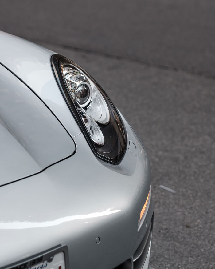 Close-up of car headlight on silver sports car parked on road