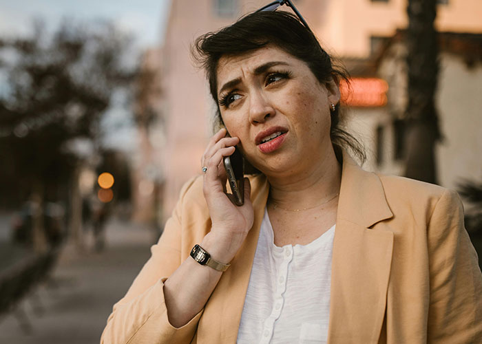 Woman outdoors talking on phone with confused, concerned look.