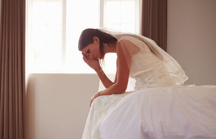 Bride in wedding dress sitting on bed upset before ceremony