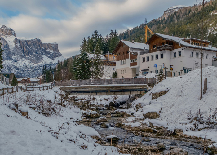 Snowy Italian hotel and bridge over stream with mountains in background Snowy Italian hotel and bridge over stream with mountains in background
