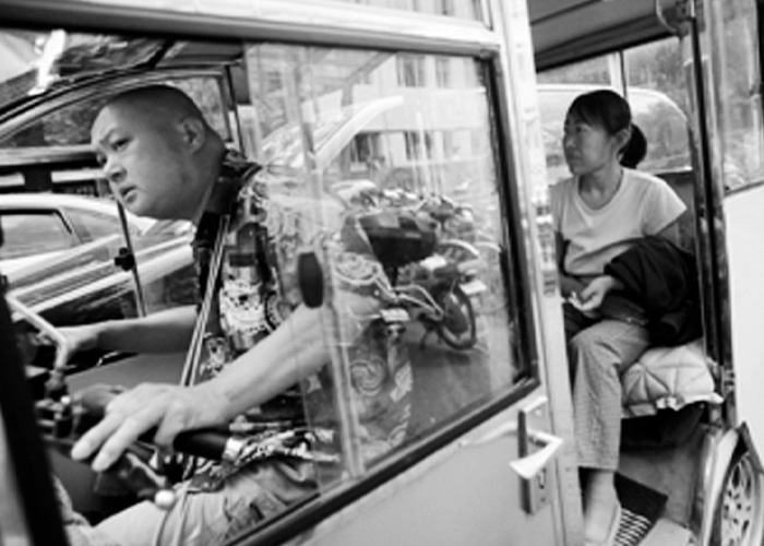 Black and white image of husband driving a small vehicle with wife seated in back Black and white image of husband driving a small vehicle with wife seated in back