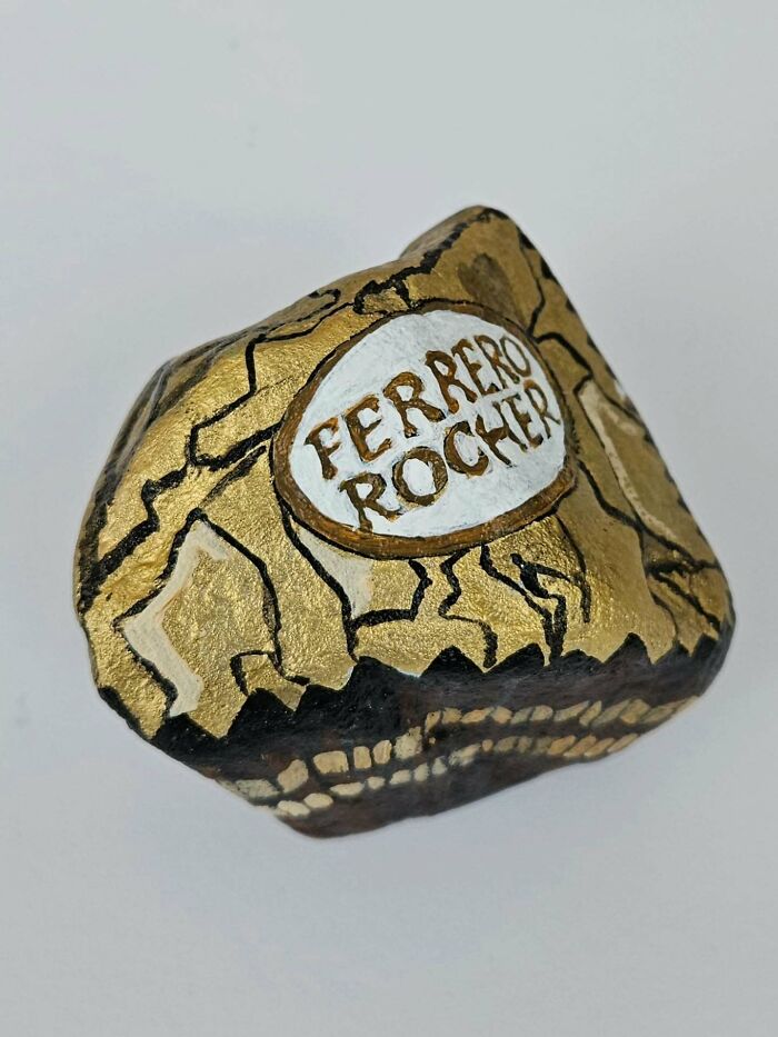 A colorful stone creation resembling a Ferrero Rocher chocolate, with a gold wrapper and white label, as an iconic food.