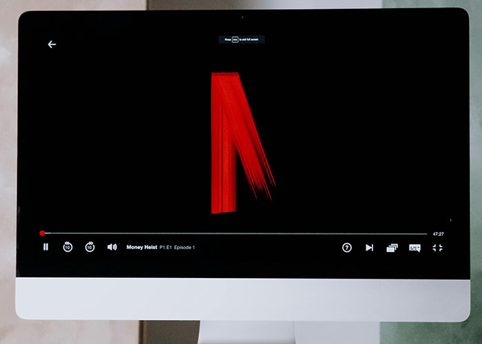A computer screen displaying a Netflix video player with the show Money Heist. People worry about the economy.