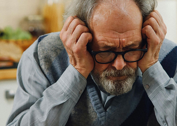 Worried elderly man holding his head in his hands