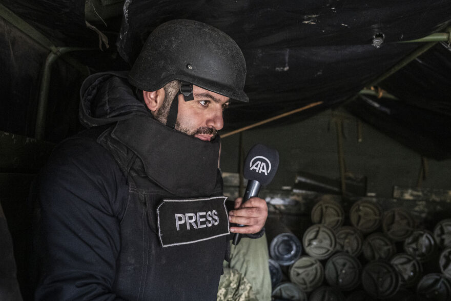 A war correspondent, wearing a helmet and a flak jacket with "PRESS" on it, holding a microphone. An example of stressful jobs.
