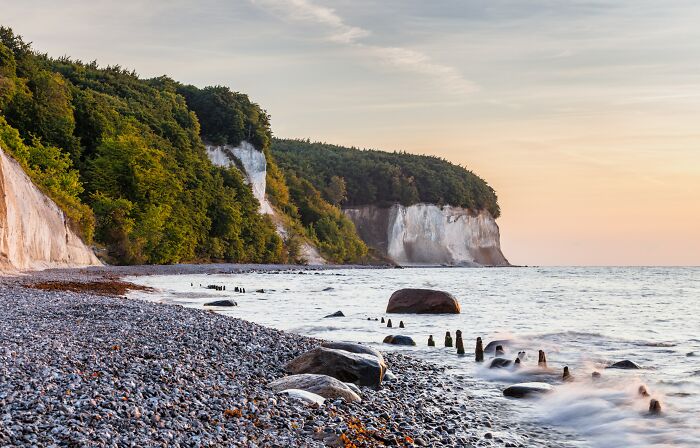 Stunning pebble beach with white cliffs and forested hills at sunset