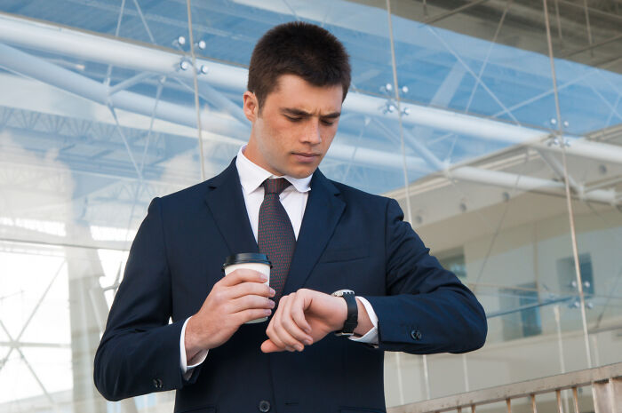 Man in suit holding coffee cup checking time on wristwatch outdoors
