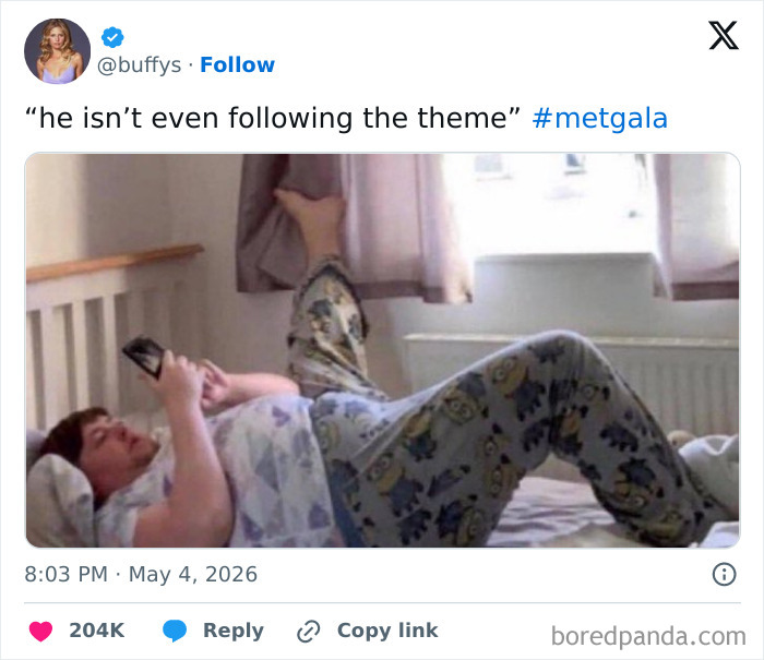 A man in pajamas lies on his back, leg up on the window, using his phone. A funny Met Gala reaction.