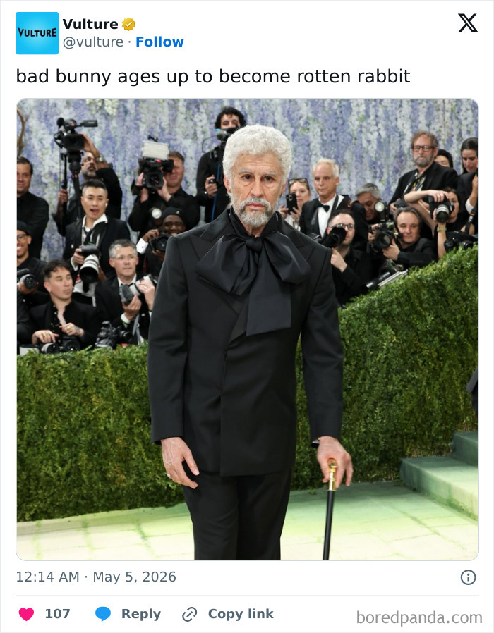 An aged Bad Bunny look-alike in a black suit with a large bow tie and cane, surrounded by photographers at the MET Gala.