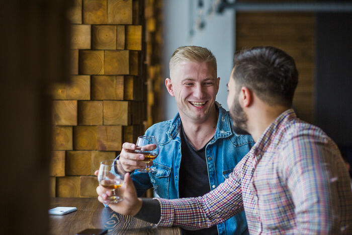 Two men clinking glasses and laughing in a cozy bar