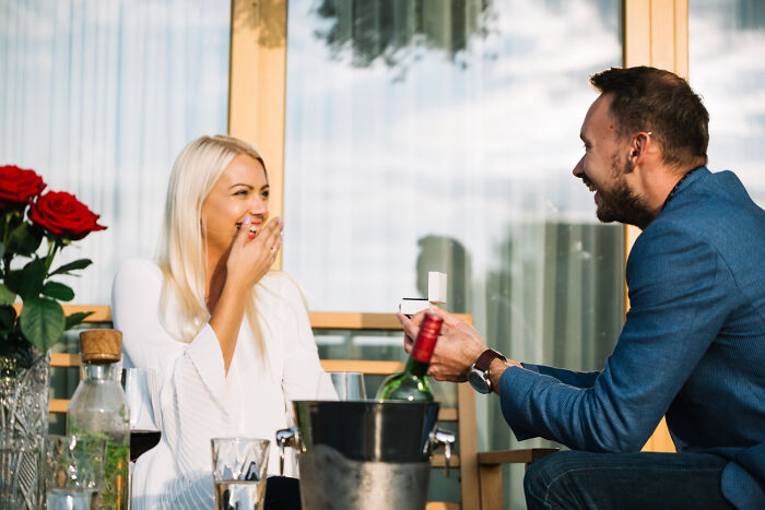 Man proposing with a ring box to a surprised woman on a balcony, embodying hilarious engagement stories.