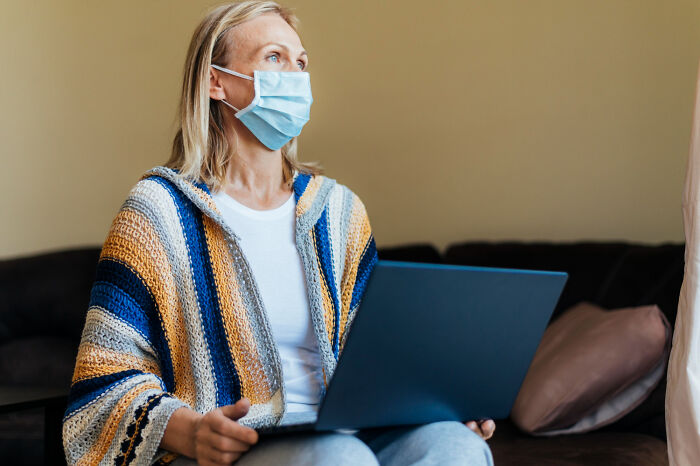 Woman wearing face mask using laptop indoors depicting conspiracy theory moments explained by facts