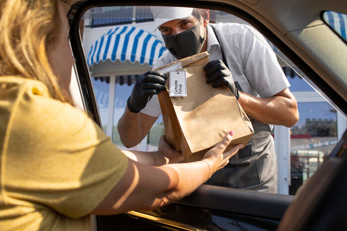 Masked worker handing paper bag to customer in car for contactless pickup