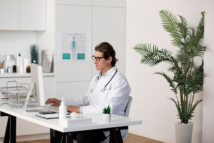 A doctor in a white coat and glasses works at a computer, discussing stories that will stay with you.