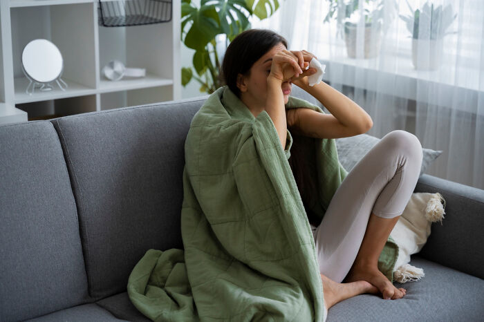 A woman wrapped in a green blanket on a couch, holding a tissue to her face, crossing to the other side of emotions.