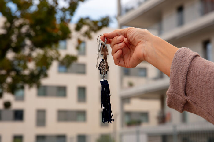 Hand holding house keys with tassel in front of apartment buildings
