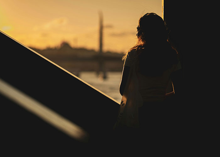 Silhouette of woman at sunset overlooking water reflecting mysterious vanishings theme