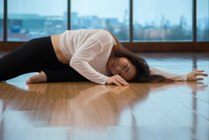 A woman on a wooden floor in a stretching pose, looking at the camera. She's crossing to the other side of her wellness journey.
