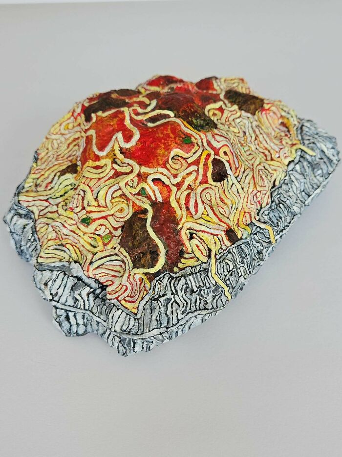 Colorful stone creation: a rock painted like spaghetti and meatballs in red sauce, a unique food art sculpture.