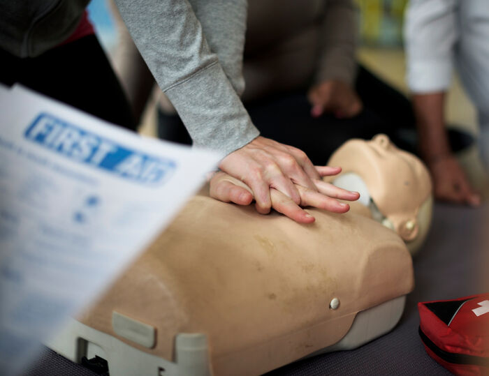 Hands perform CPR on a mannequin during a First Aid course. Learning life-saving skills to help people cross to the other side.