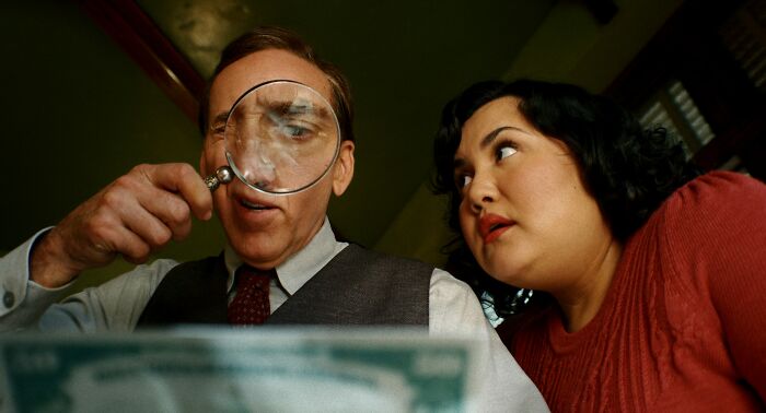 Man examining paper with magnifying glass beside woman close-up scene Man examining paper with magnifying glass beside woman close-up scene