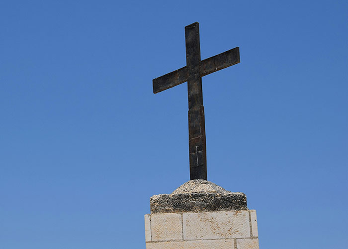 Old cross on stone pedestal against blue sky symbolizing mysterious vanishings