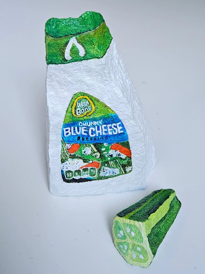 A stone creation painted as a Wish-Bone Chunky Blue Cheese dressing bottle and a lime wedge. The artist turns rocks into iconic foods and famous products.