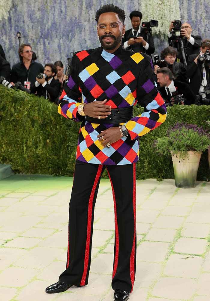 A man in a colorful geometric patterned jacket and black pants with red stripes, posing at Met Gala 2026. Worst dressed stars.