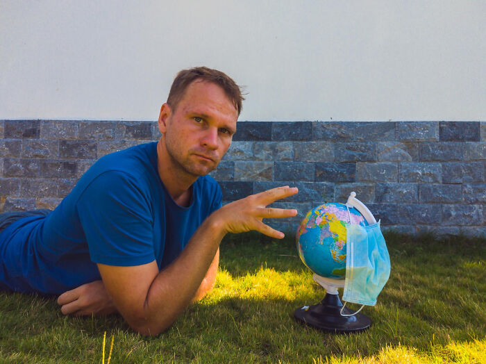 Man lying on grass next to globe with face mask