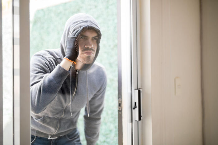 Man in hoodie peering through glass door showing January 6 surprise