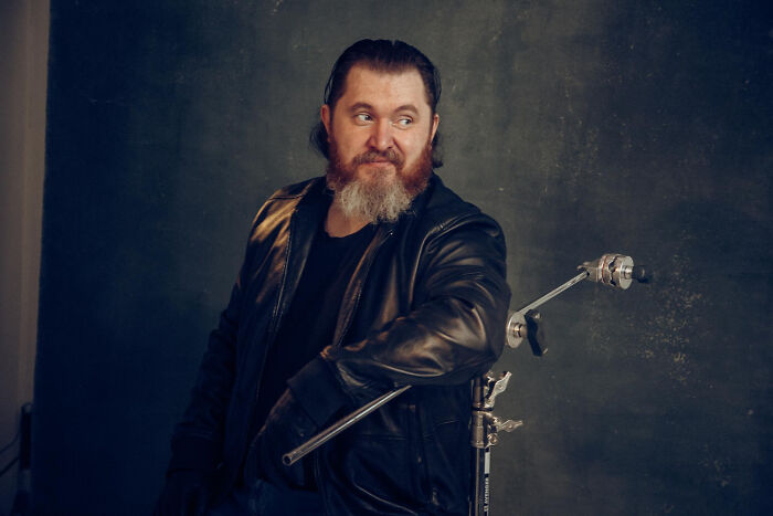 A man with a full beard and black leather jacket smiles, looking away from the camera. Celebrity relatives.