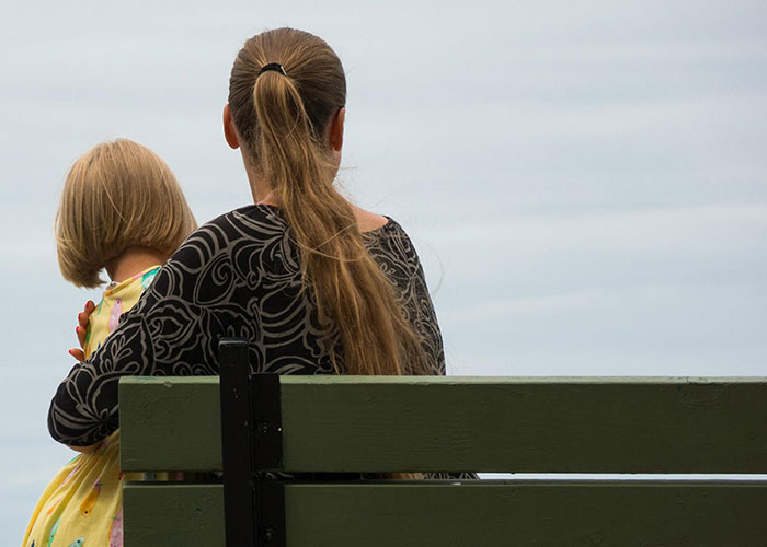 Woman with long hair sitting on bench with child outdoors
