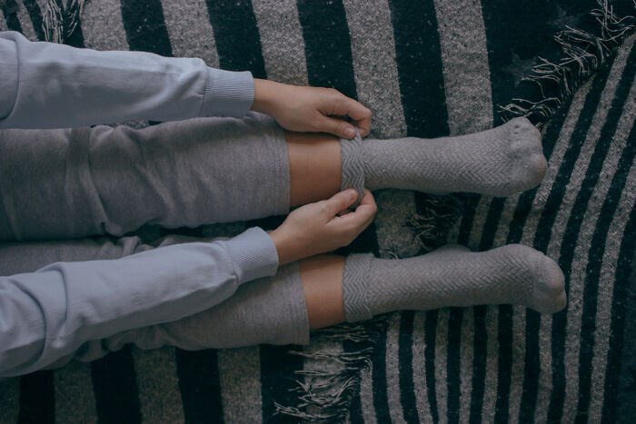 Person adjusting cozy socks while resting on striped blanket