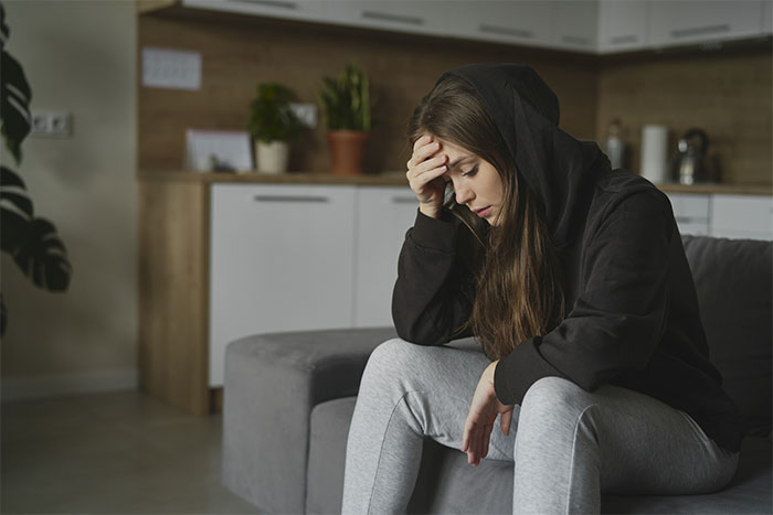 Young woman in a black hoodie and gray sweatpants, head in hand, looking distressed, conveying a family conflict about a grandchild and circumcision.