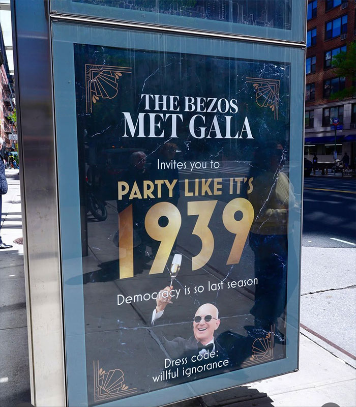 A "MET Gala" protest poster on a bus stop, featuring Jeff Bezos and text about partying like 1939.