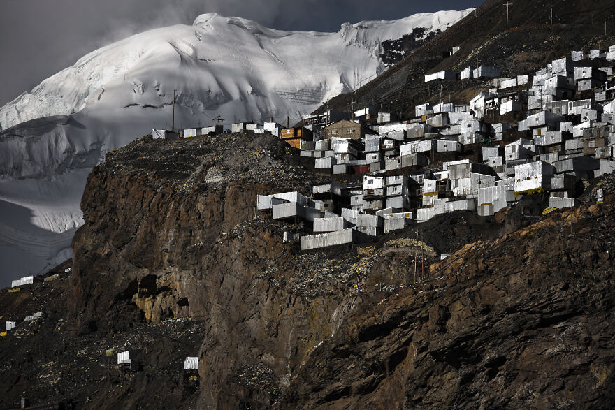A village of shipping containers on a rugged mountainside, with a snow-capped peak in the background. An isolated place on Earth.