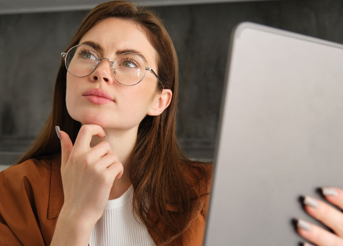 Woman in glasses, holding a tablet, looking up thoughtfully. She's considering facts that keep getting repeated on Reddit.