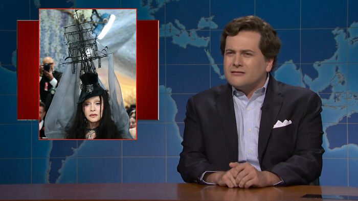 A man in a suit reacting to a woman in an elaborate ship-hat outfit. Met Gala outfits and Statue of Liberty in a burqa. A man in a suit reacting to a woman in an elaborate ship-hat outfit. Met Gala outfits and Statue of Liberty in a burqa.