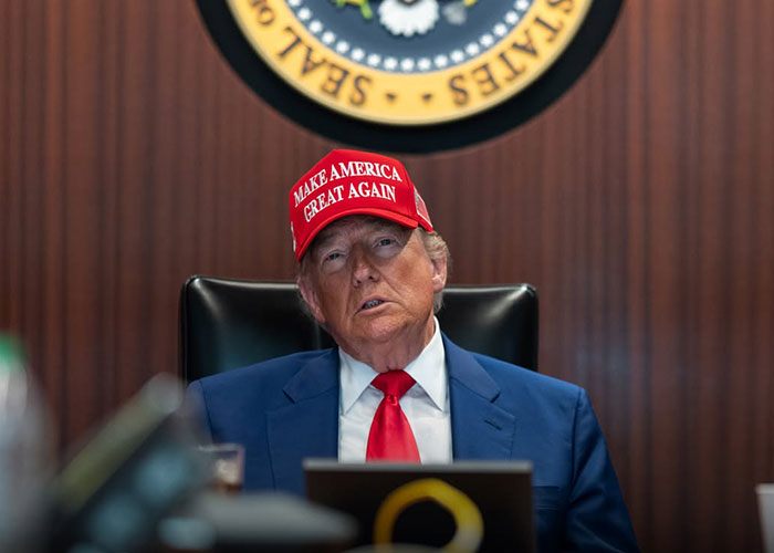 President Trump wearing a Make America Great Again hat at a desk President Trump wearing a Make America Great Again hat at a desk