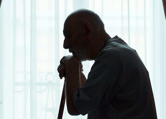 Silhouette of elderly man leaning on cane inside a room