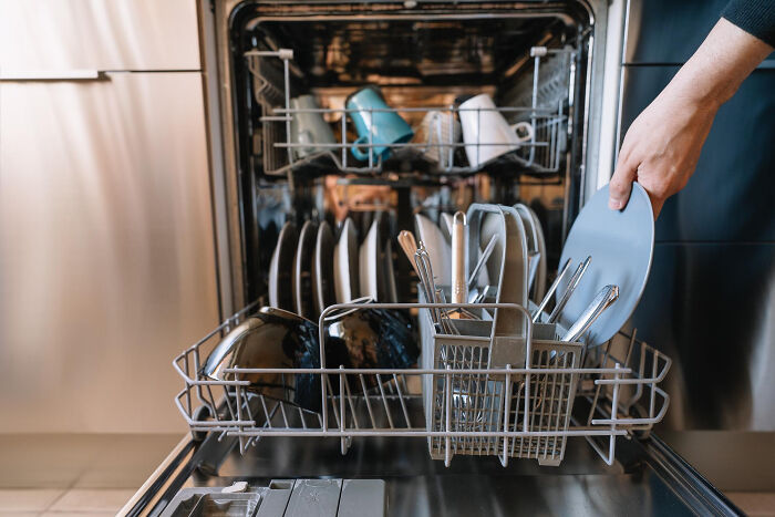 Person loading dishes into a dishwasher with plates and utensils