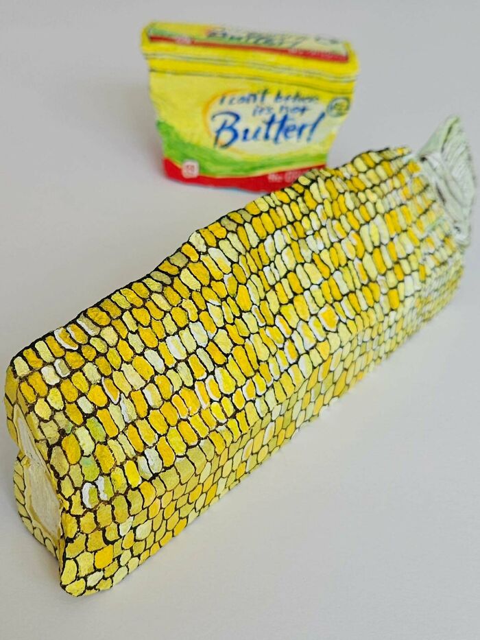 Colorful stone creation of a corn on the cob next to a painted container of I Can't Believe It's Not Butter.