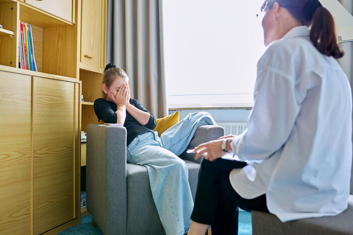 Distressed teenager covering face during counseling at psychiatric facility