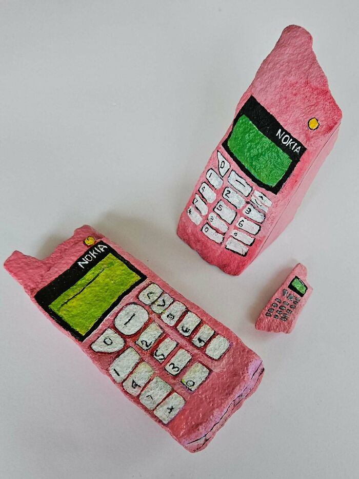 Two colorful stone creations, painted as pink Nokia phones with green screens, alongside a tiny matching one.