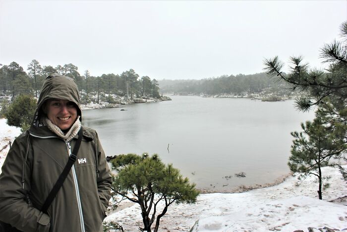 Smiling person in winter clothing near a calm lake with stunning snow-covered views