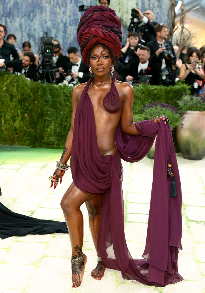 Worst dressed star at Met Gala 2026. A woman in a sheer, draped plum gown and an elaborate headpiece.