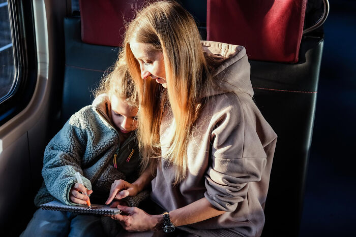 A mother and child coloring in a notebook on a train, illuminated by sunlight. No second-hand embarrassment here!