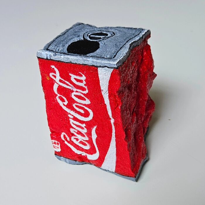 A colorful stone creation shaped like a crushed Coca-Cola can, a creative rock art piece transforming iconic foods.
